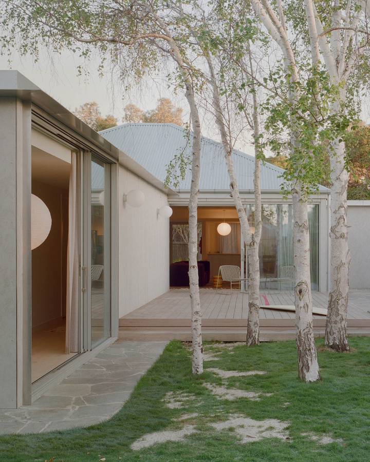 A white rendered addition with sliding doors onto a deck, with silver birches on the lawn in front.