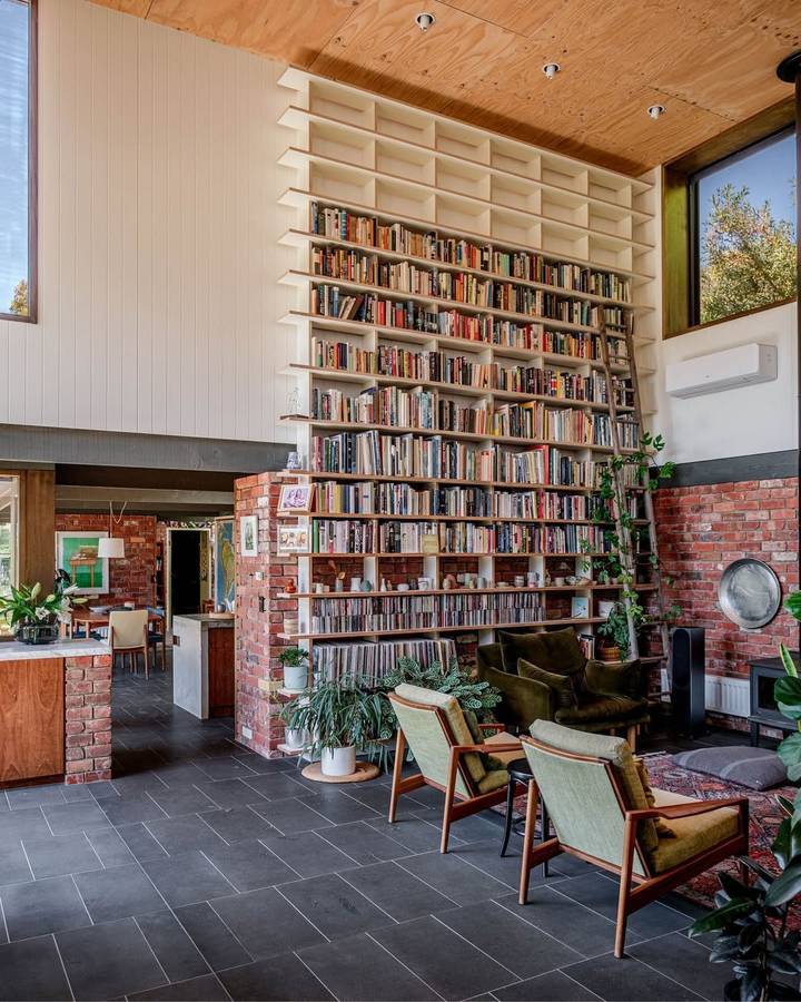 A double height living room with a full height library wall of books and records above brick piers.