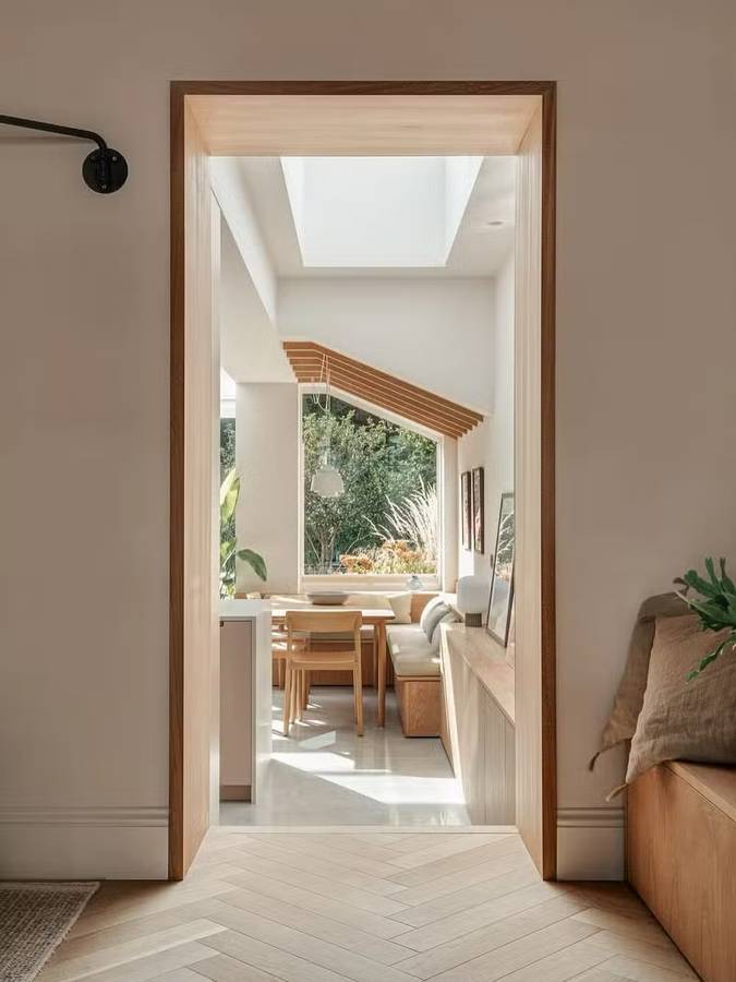 A view through a doorway to a dining nook with timber beams, a skylight and a bench seat under a garden window.