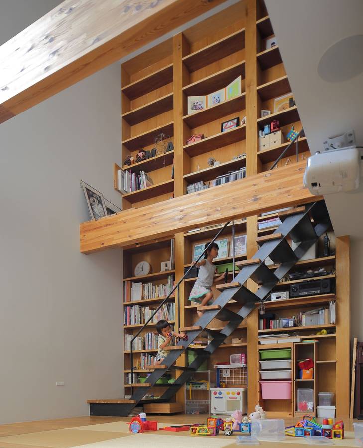 A double height timber bookshelf wall with a black steel stair running up it, above a tatami floor.