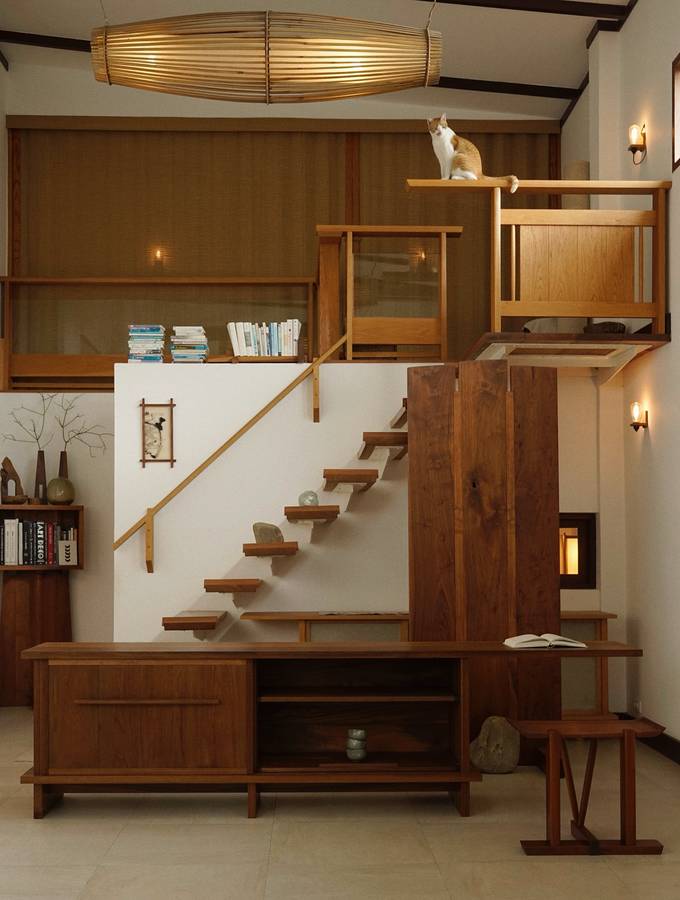 A teak sideboard below a floating timber stair, with a cat sitting on a high shelf above.